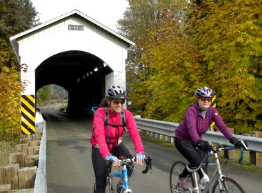 Bicyclists Riding Past A Covered Bridge