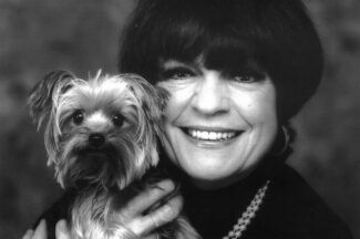 A woman smiles while holding her small dog to pose for a portrait.