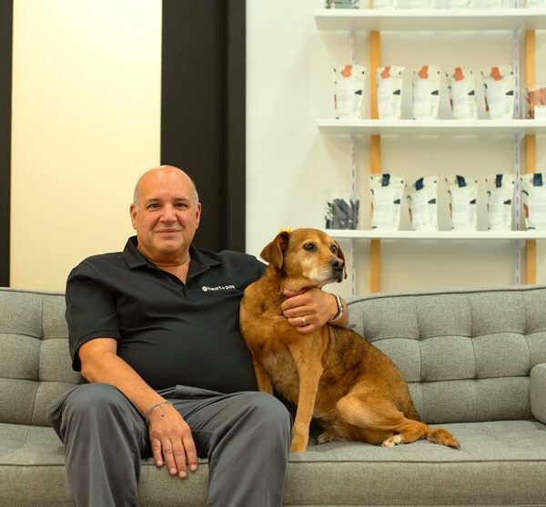 A middle-aged man sits on a couch with a brown dog.